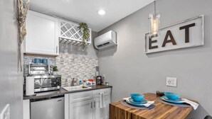 A compact kitchen with white cabinets, a wooden dining table, and a wall-mounted 'EAT' sign.
