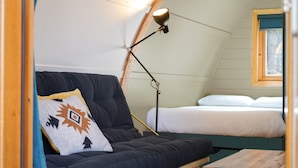 A cozy room with a dark-colored sofa, a bedside table, a lamp, and a bed with white bedding. - Deluxe Cosy Cabin in the Scottish Highlands (Tomintoul)