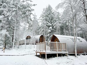 A row of log cabins with wooden decks and railings, surrounded by snow-covered trees. - Deluxe Cosy Cabin in the Scottish Highlands (Tomintoul)