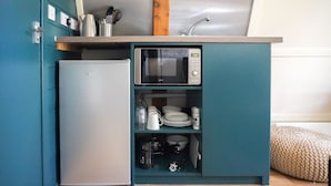 A compact kitchenette with a built-in microwave, a small refrigerator, and a shelf with dishes and utensils. - Deluxe Cosy Cabin in the Scottish Highlands (Tomintoul)
