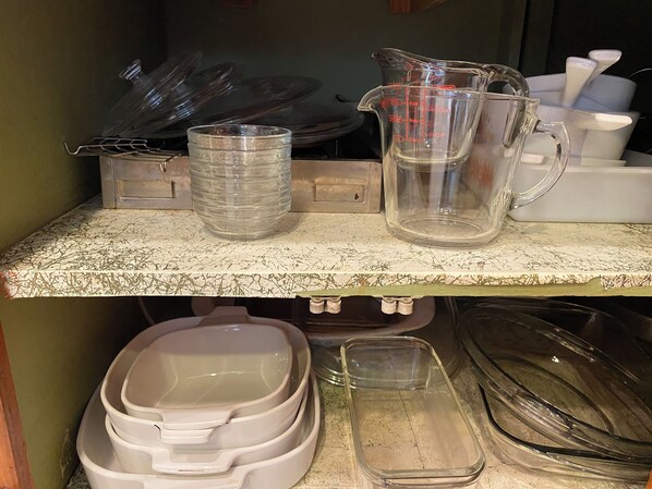 Una encimera de cocina con varios vasos, incluyendo una pila de vasos transparentes, un jarro medidor y una jarra de cristal.