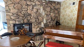 A dining area with a stone wall, a fireplace, a piano, and a bench.