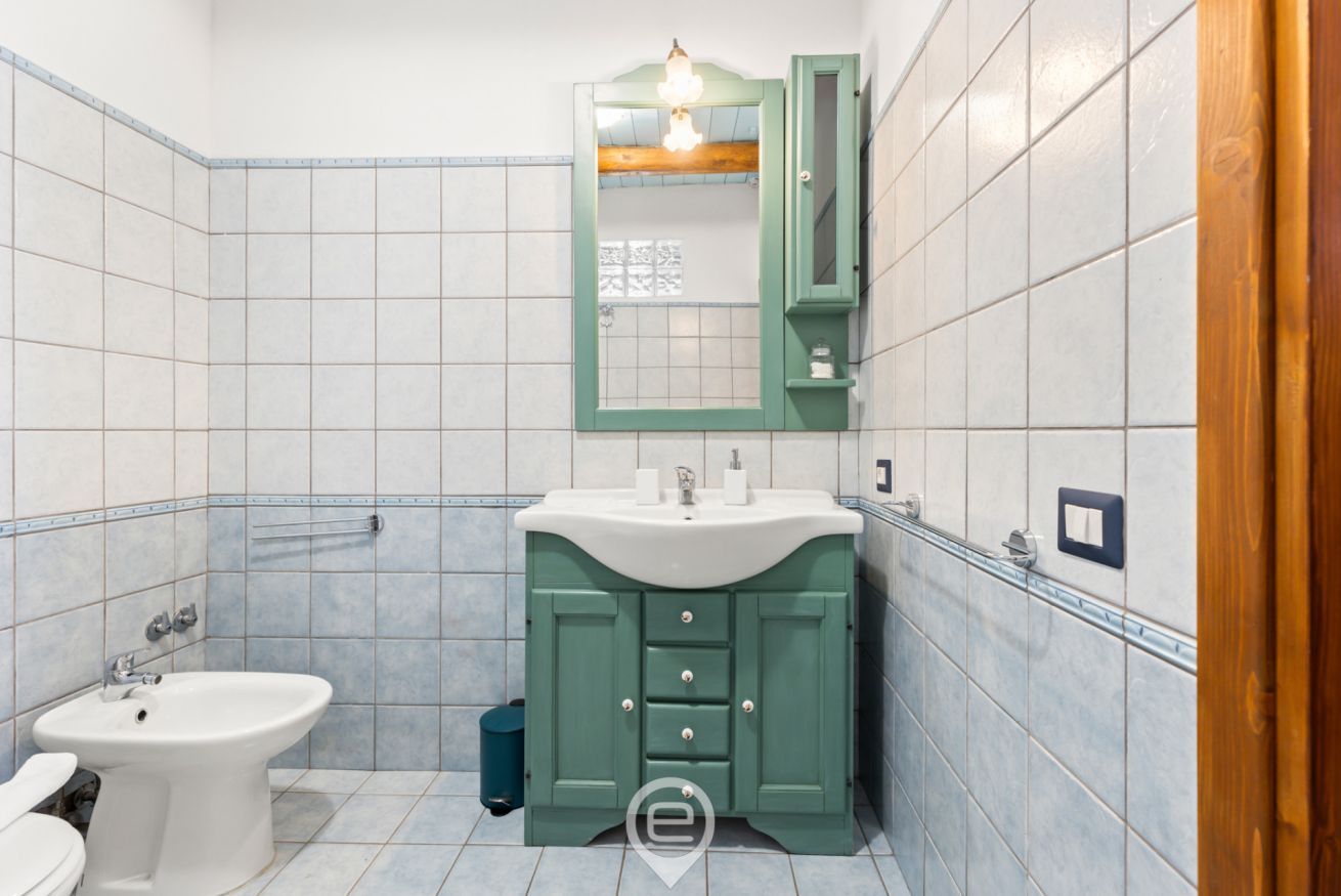 Un bany amb un lavabo pedestal blanc, un tocador verd amb mirall i un vàter blanc.