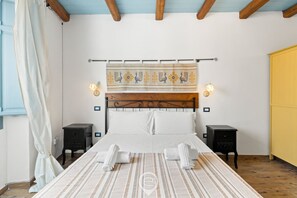 Ein Schlafzimmer mit einem Bett, zwei Nachttischen, einem Kopfteil mit einer Zierleiste und einem Vorhang links.