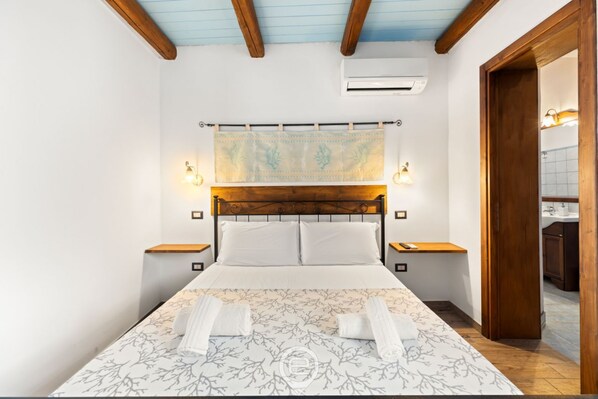 A hotel room with a wooden headboard, a large bed with white linens, two bedside tables with lamps, and a view of the bathroom through an open door.