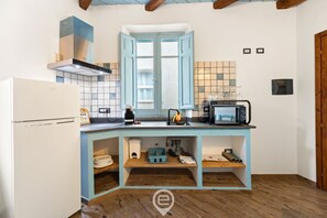 Eine Küche mit einem weißen Kühlschrank, einer blauen Arbeitsfläche, einer Mikrowelle und einem Fenster mit blauen Fensterläden.