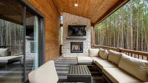 A cozy outdoor seating area with a stone fireplace, wooden deck, and glass doors leading to a patio.