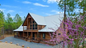 A two-story log cabin with a metal roof, a porch with railings, and a gravel driveway.