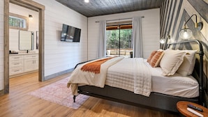 A bedroom with a bed, a ceiling fan, a TV, and a window with curtains.