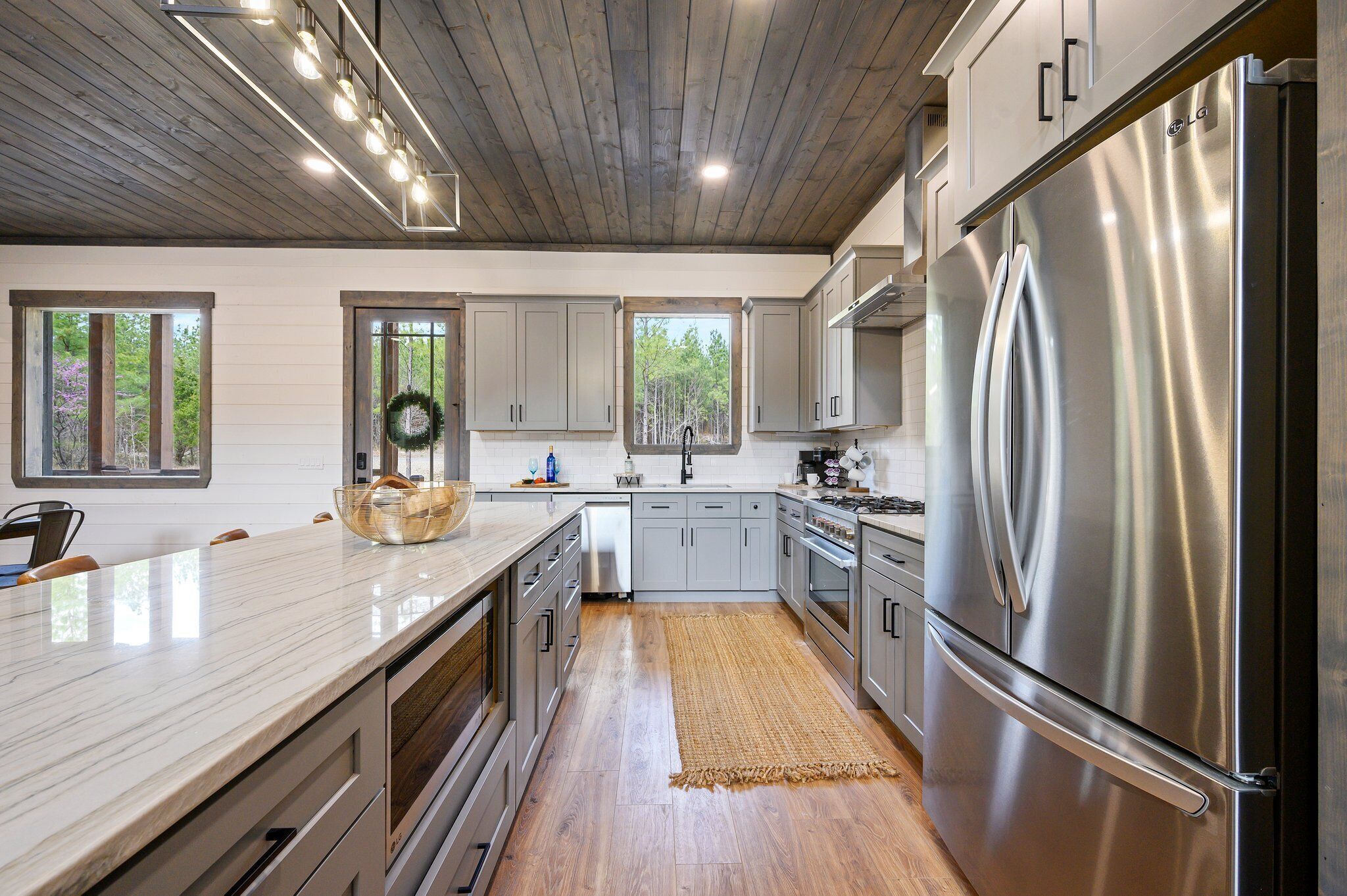 A modern kitchen with stainless steel appliances, wooden flooring, and large windows.