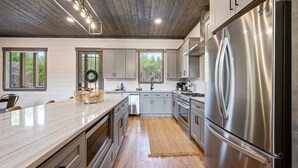 A modern kitchen with stainless steel appliances, wooden flooring, and large windows.
