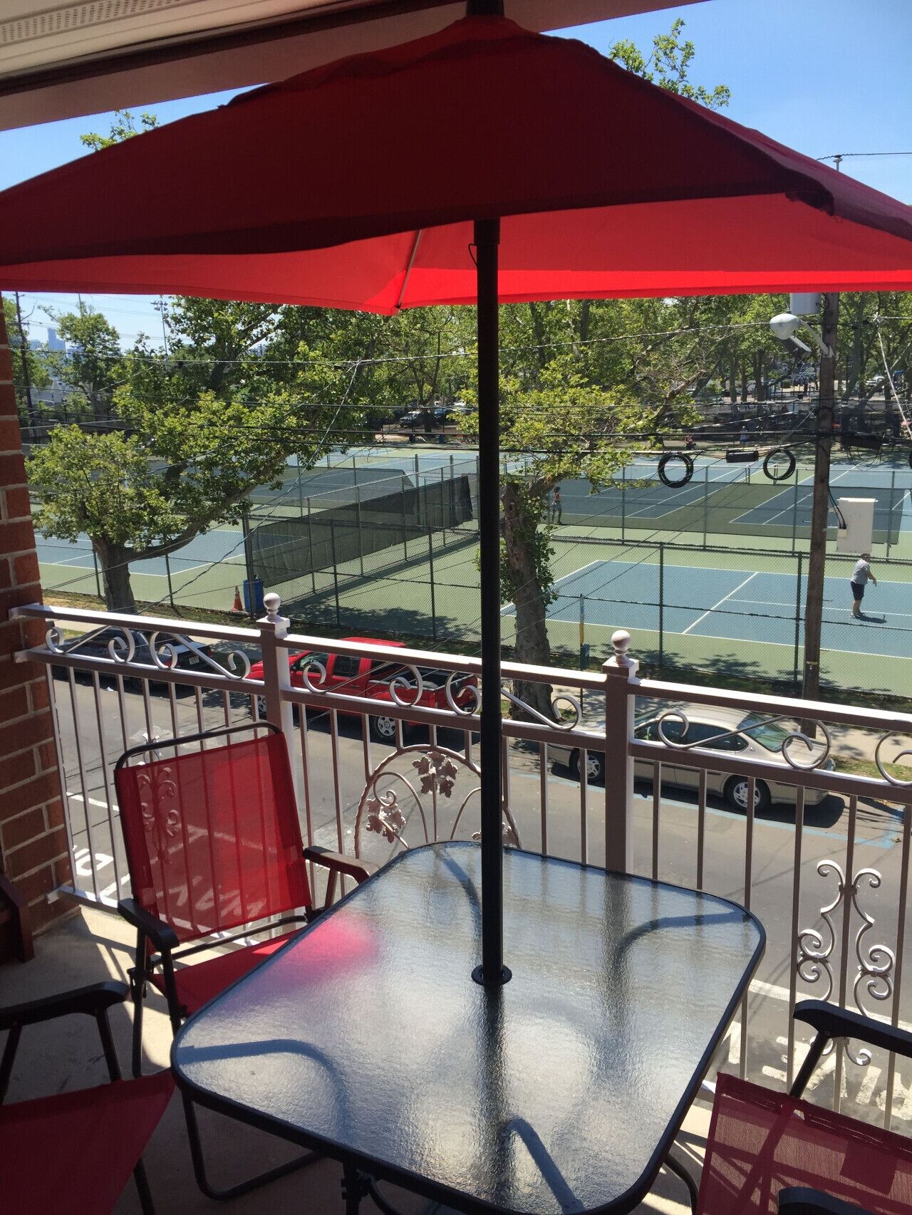 A balcony with a red umbrella, a glass table, and a red chair.