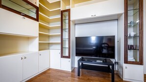 A modern living room with a flat-screen TV, wooden flooring, built-in shelving, and a glass-fronted cabinet. - YiD Amaryllis (Firenze)