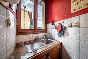 Una cocina con ventana, azulejos blancos, un lavamanos y una pared roja.