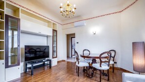 A living room with a flat-screen TV, wooden dining table, and chairs. - YiD Amaryllis (Firenze)