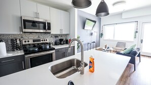 A modern kitchen with a central island, stainless steel appliances, and a flat-screen TV mounted on the wall.
