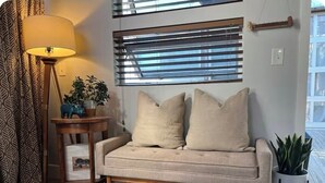 A beige sofa with two cushions, a floor lamp, a small table with a plant, and a window with blinds. - Charming 1-bedroom apartment with WiFi, AC in wonderful Denver (Denver)