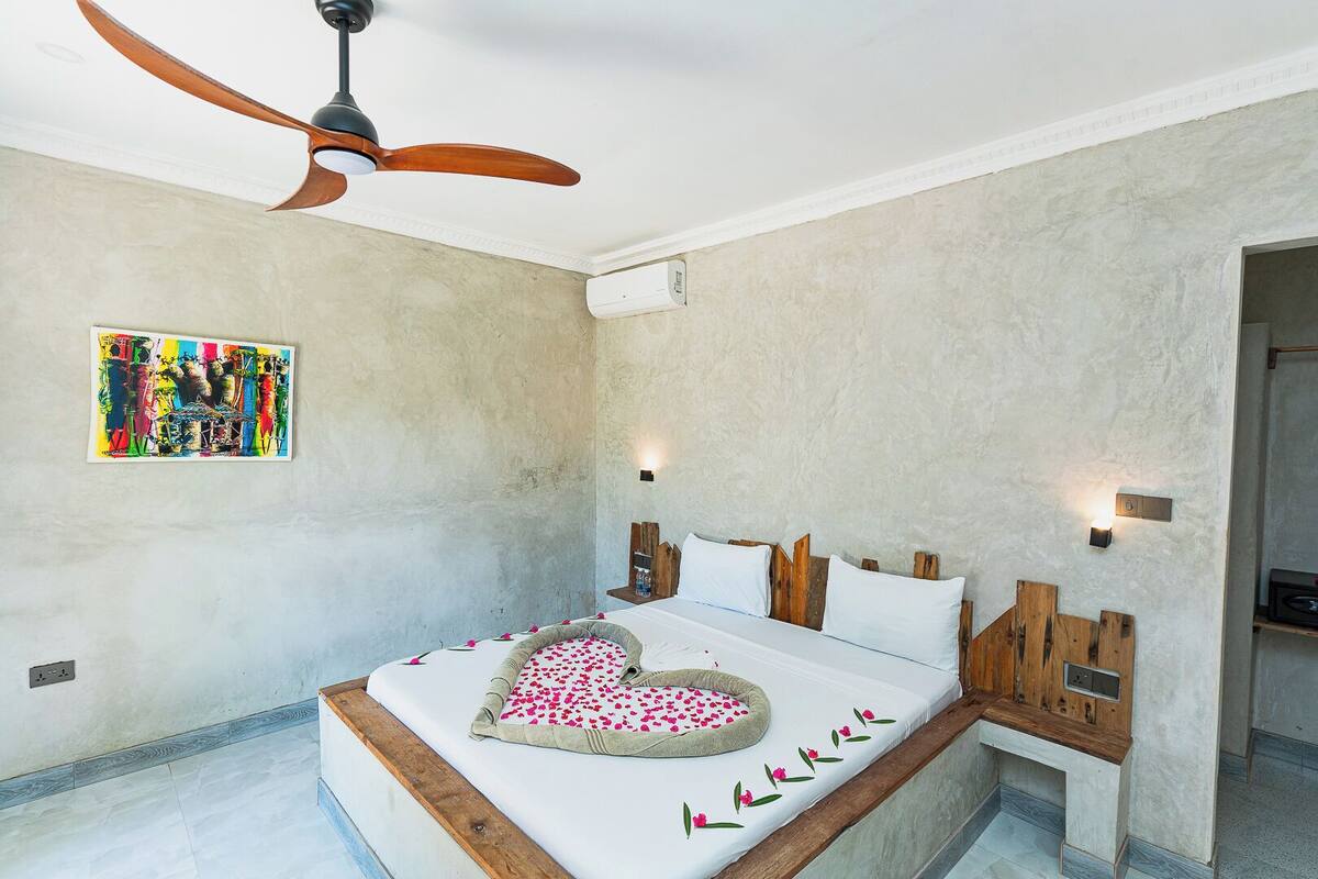 Un dormitorio con cama, ventilador de techo, luz en la pared y un cuadro.