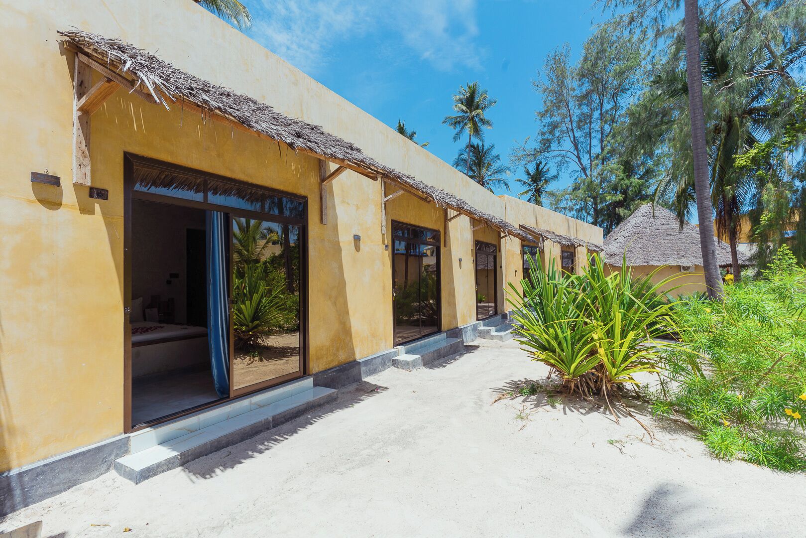 A resort building with multiple rooms, each with a thatched roof entrance and a view of the surrounding greenery.