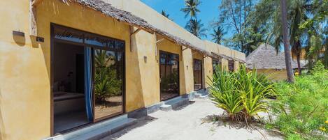 A resort building with multiple rooms, each with a thatched roof entrance and a view of the surrounding greenery.