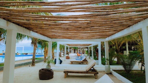 Un salon de plage doté d’un toit de chaume, de chaises longues et d’une piscine.