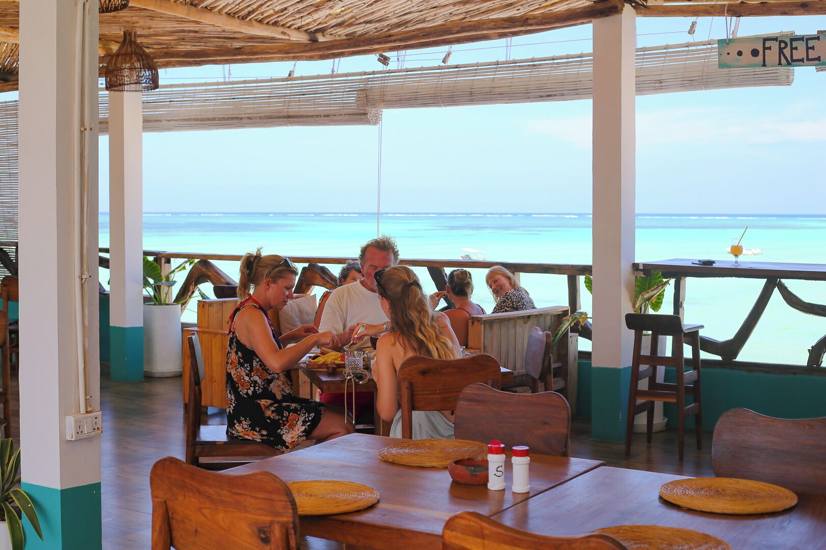 A restaurant with outdoor seating overlooking the sea, wooden tables, and a thatched roof.