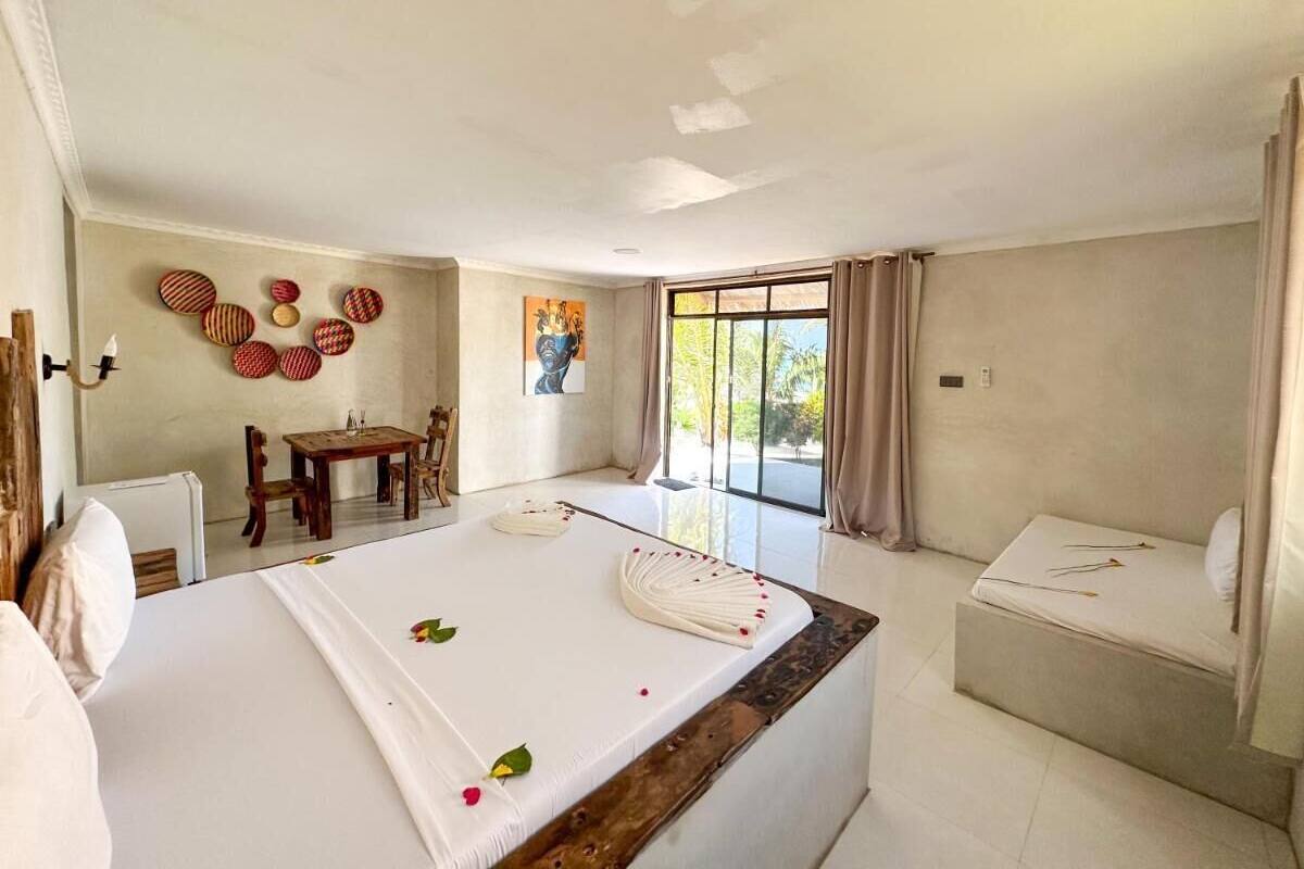 Habitación de hotel con cama, una mesita, una silla, ventana con cortinas y un cuadro en la pared.