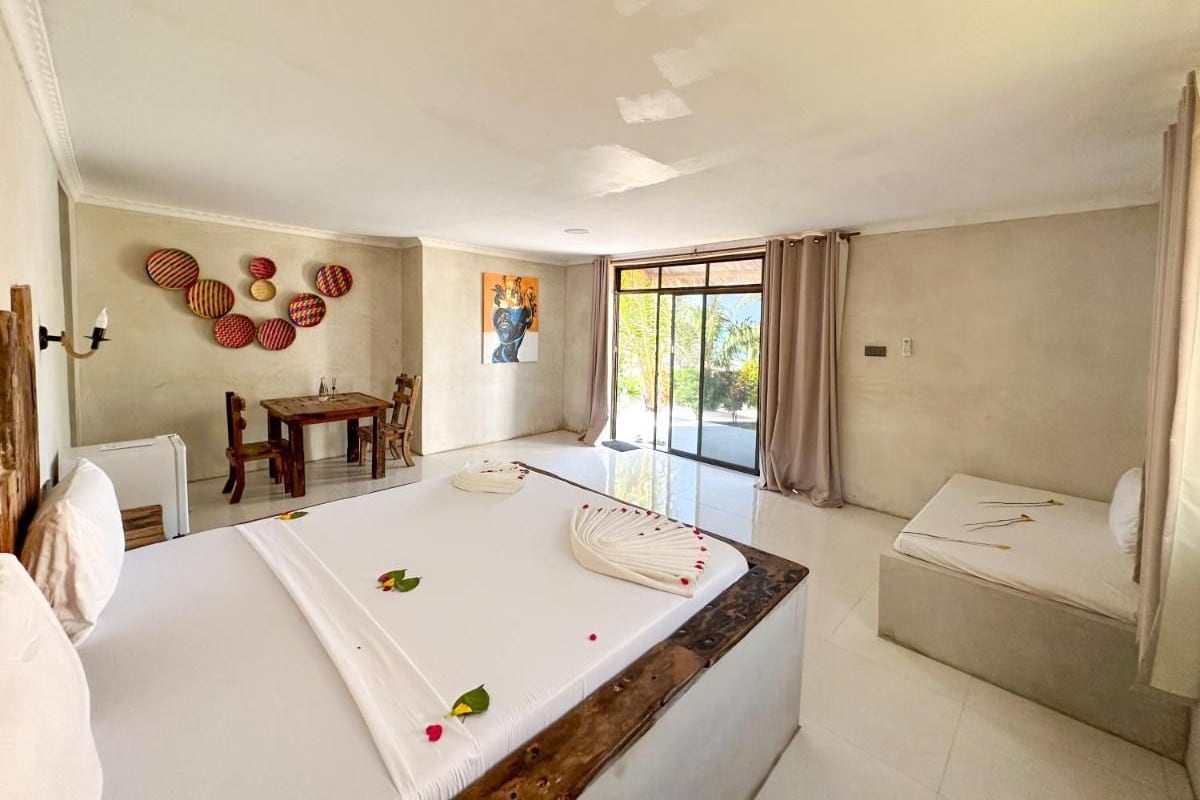 Habitación de hotel con cama, una mesita, una silla, ventana con cortinas y un cuadro en la pared.