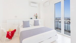 Une chambre moderne avec un grand lit, des murs blancs et un balcon offrant une vue sur le port de plaisance.