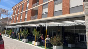A multi-story building with a brick facade, balconies, and a covered outdoor seating area with potted plants. - BENNINGTON (Elche)