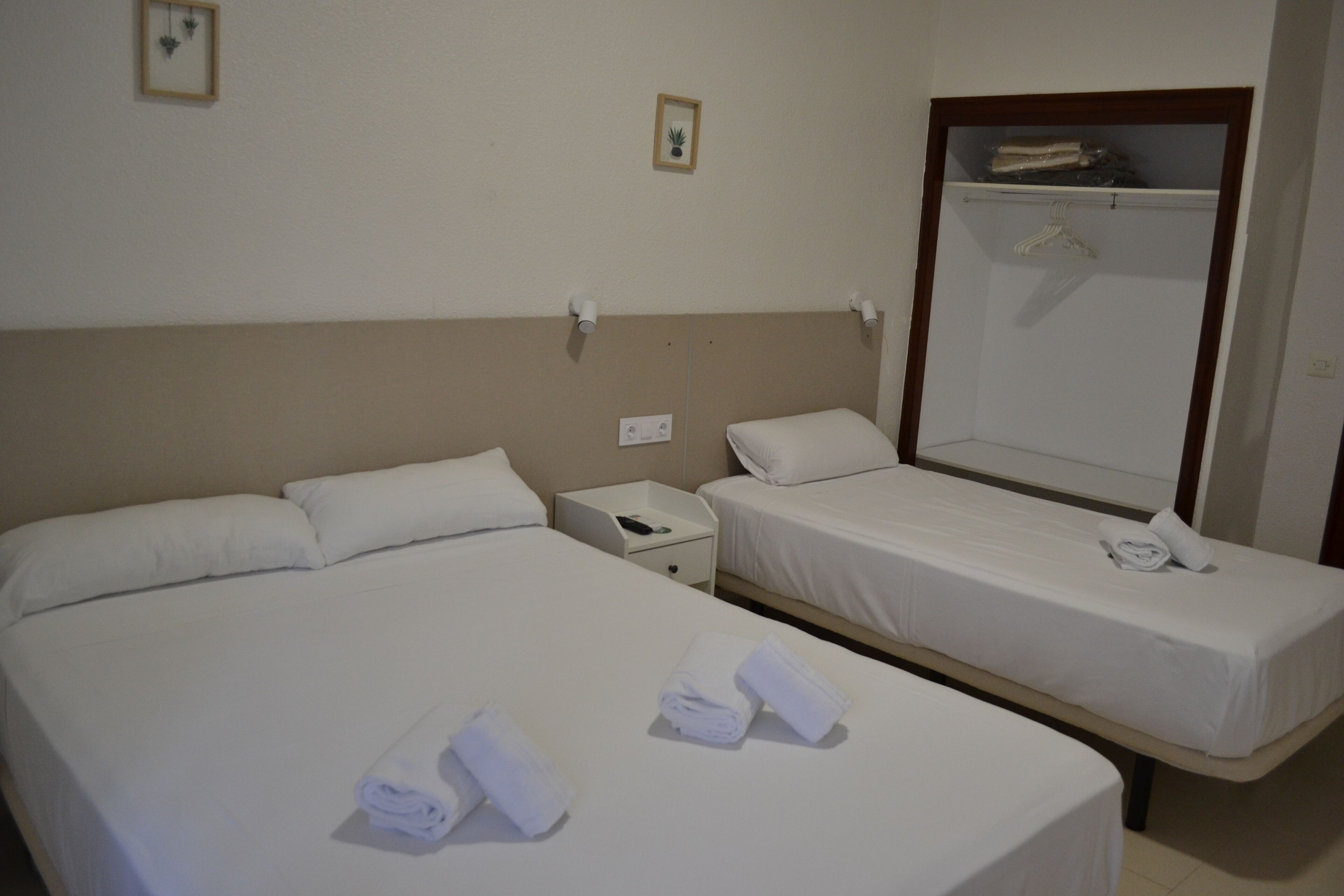 Ett hotellrum med två sängar, båda med vita sängkläder och handdukar. Det finns ett litet nattduksbord med en telefon och ett eluttag.