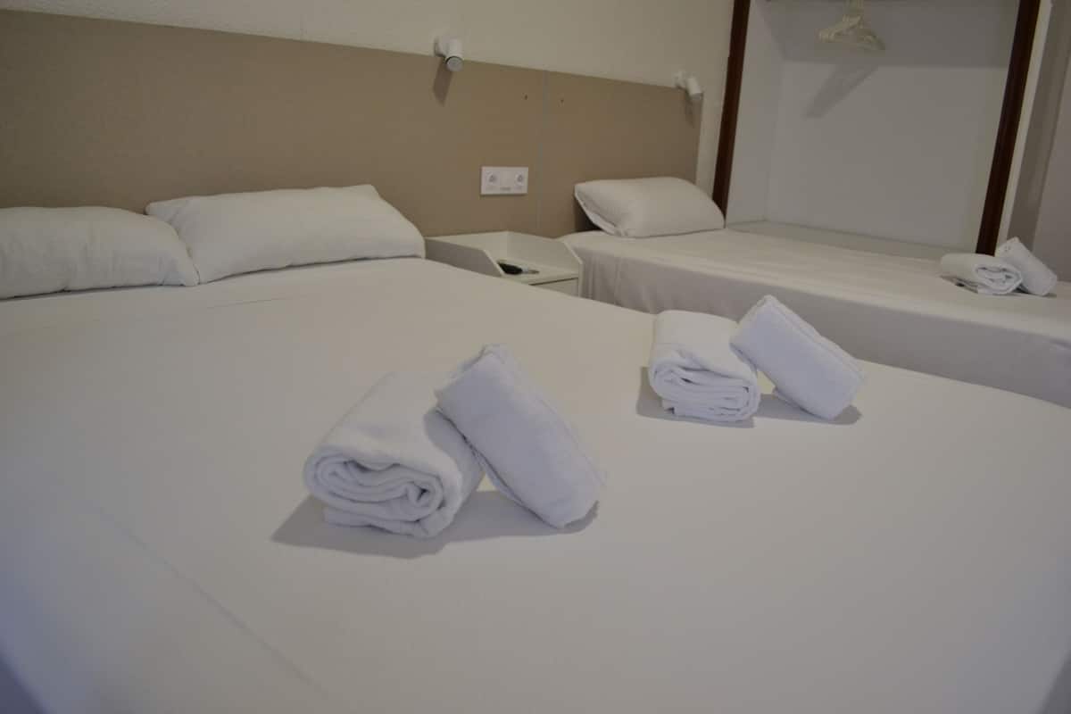 A hotel room with two beds, each with white linens and pillows. There are two bedside tables with lamps and a mirror.