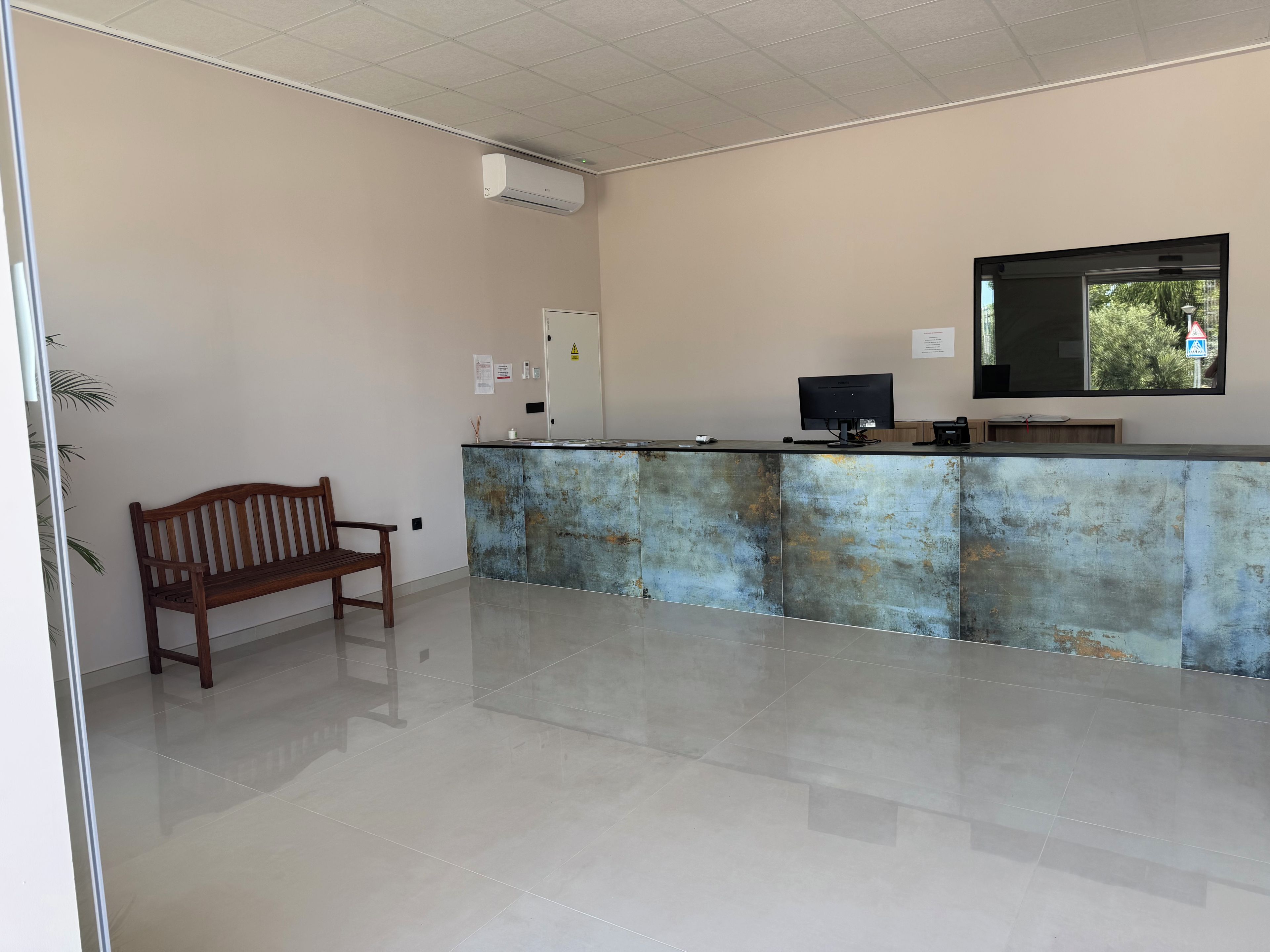 A reception area with a wooden bench, a reception desk, a flat-screen TV, and a wall-mounted air conditioner.