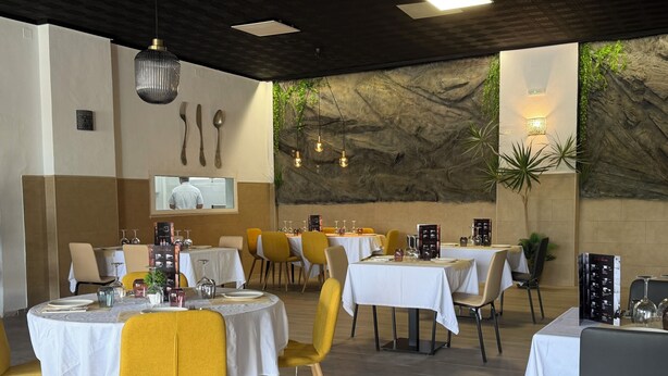 A restaurant with round tables, yellow chairs, and a stone wall with greenery. - BENNINGTON (Elche)