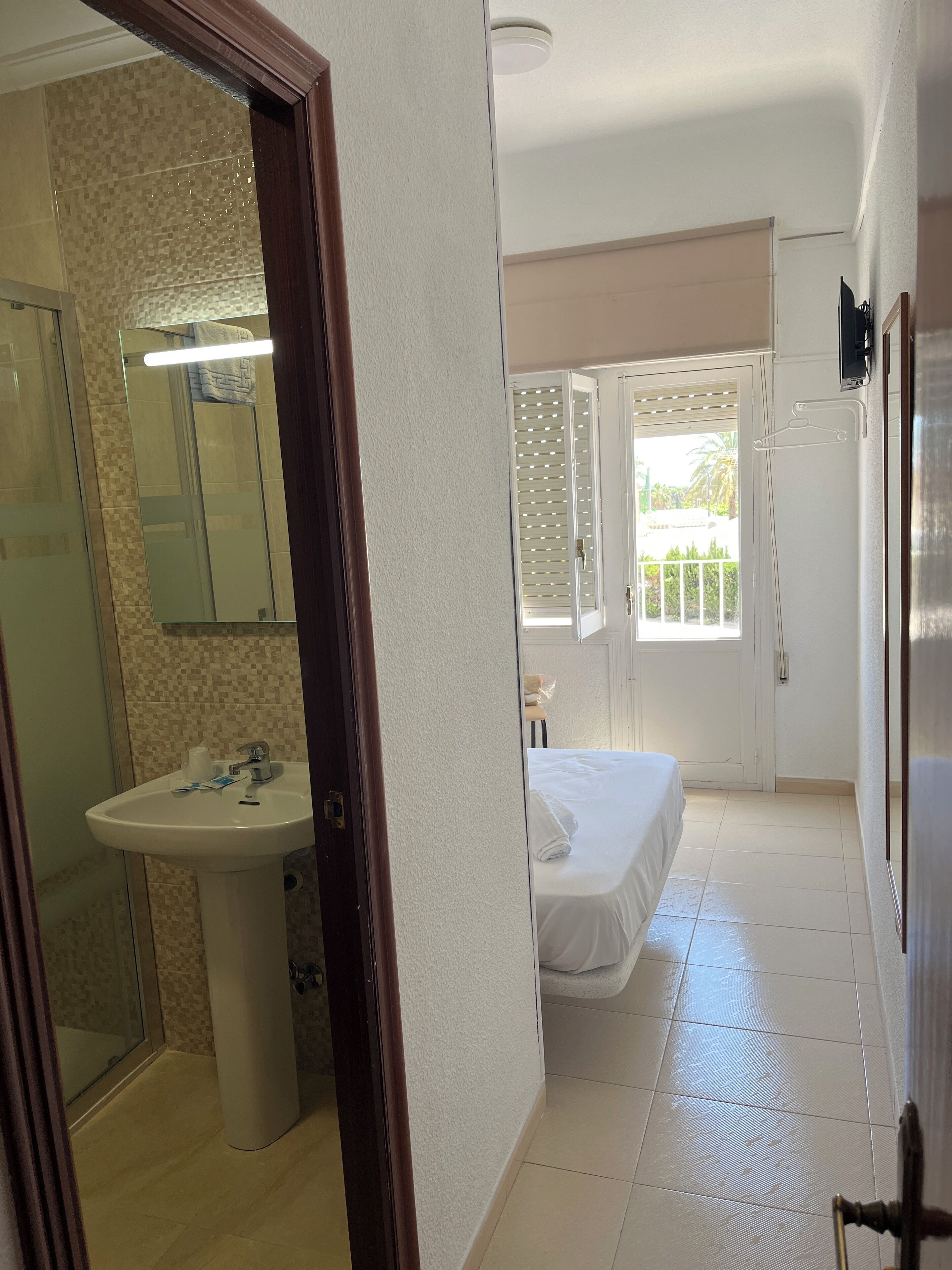 A hotel room with a bathroom, a bed, and a view of the outdoors.