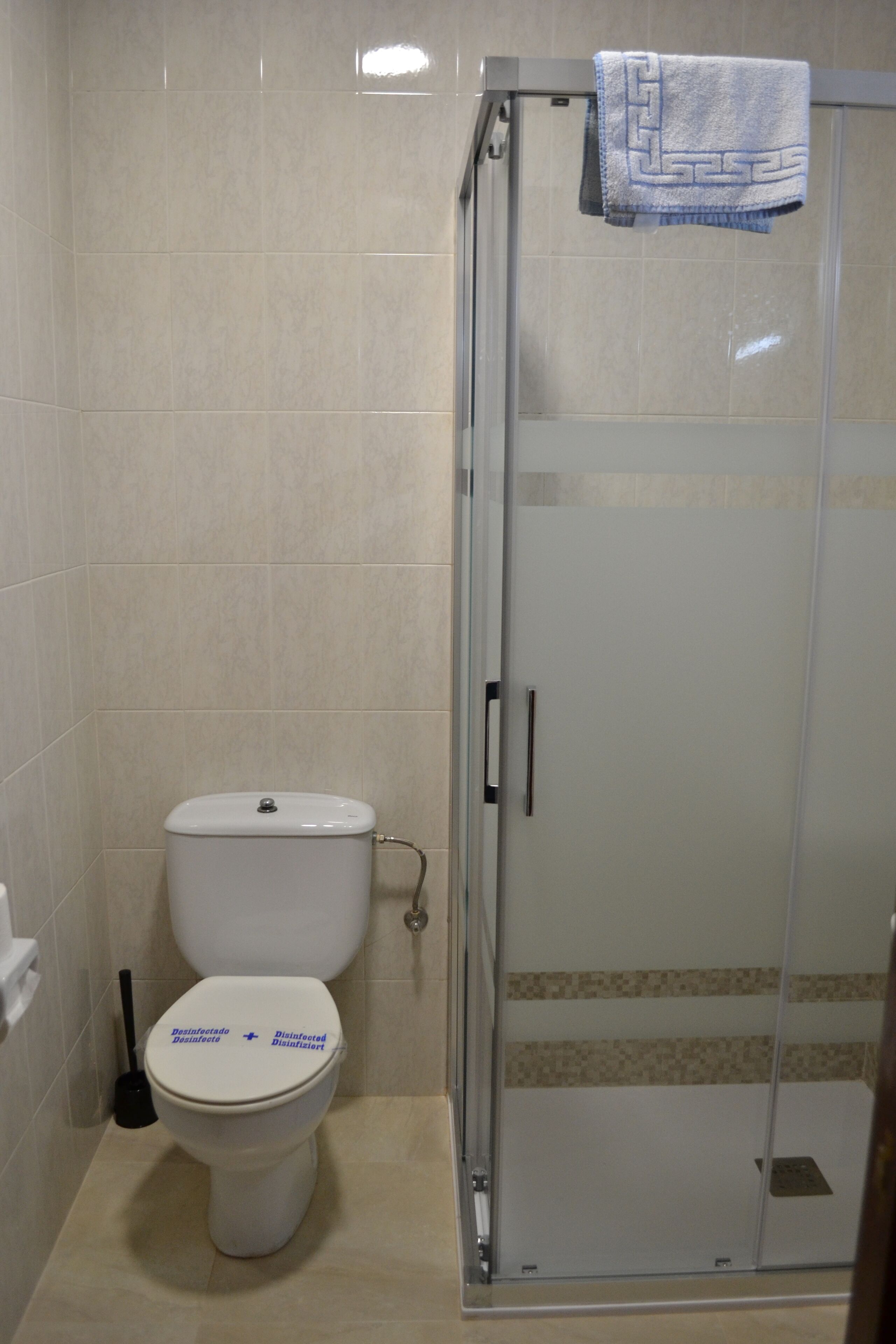 Een badkamer met een toilet, een douchecabine van glas en een handdoek aan de douchedeur.