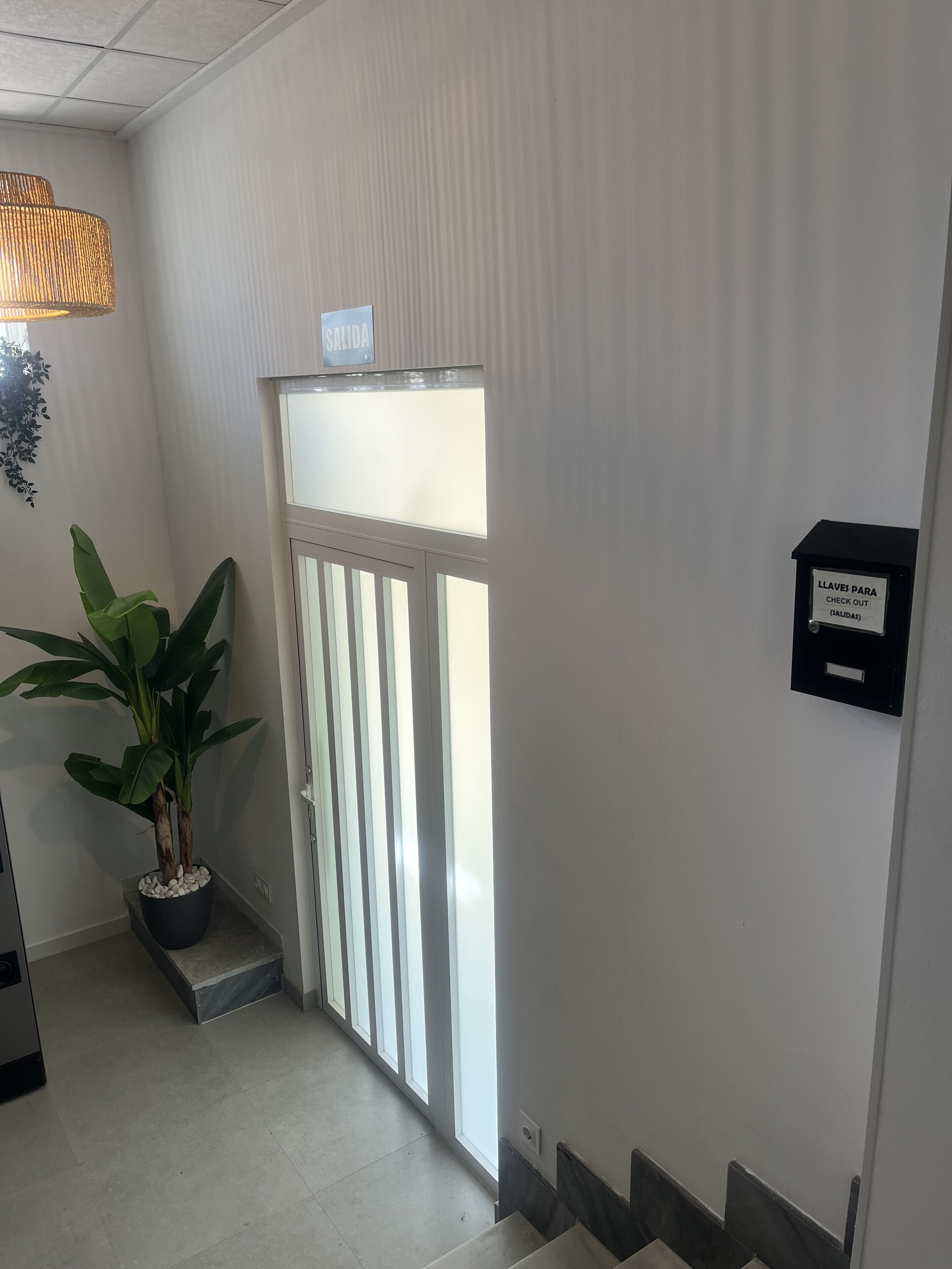 A hotel entrance with a check-out machine, a potted plant, and a sign indicating the exit.