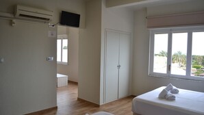 A hotel room with a bed, a TV mounted on the wall, a wardrobe, and a window with a view of palm trees. - BENNINGTON (Elche)