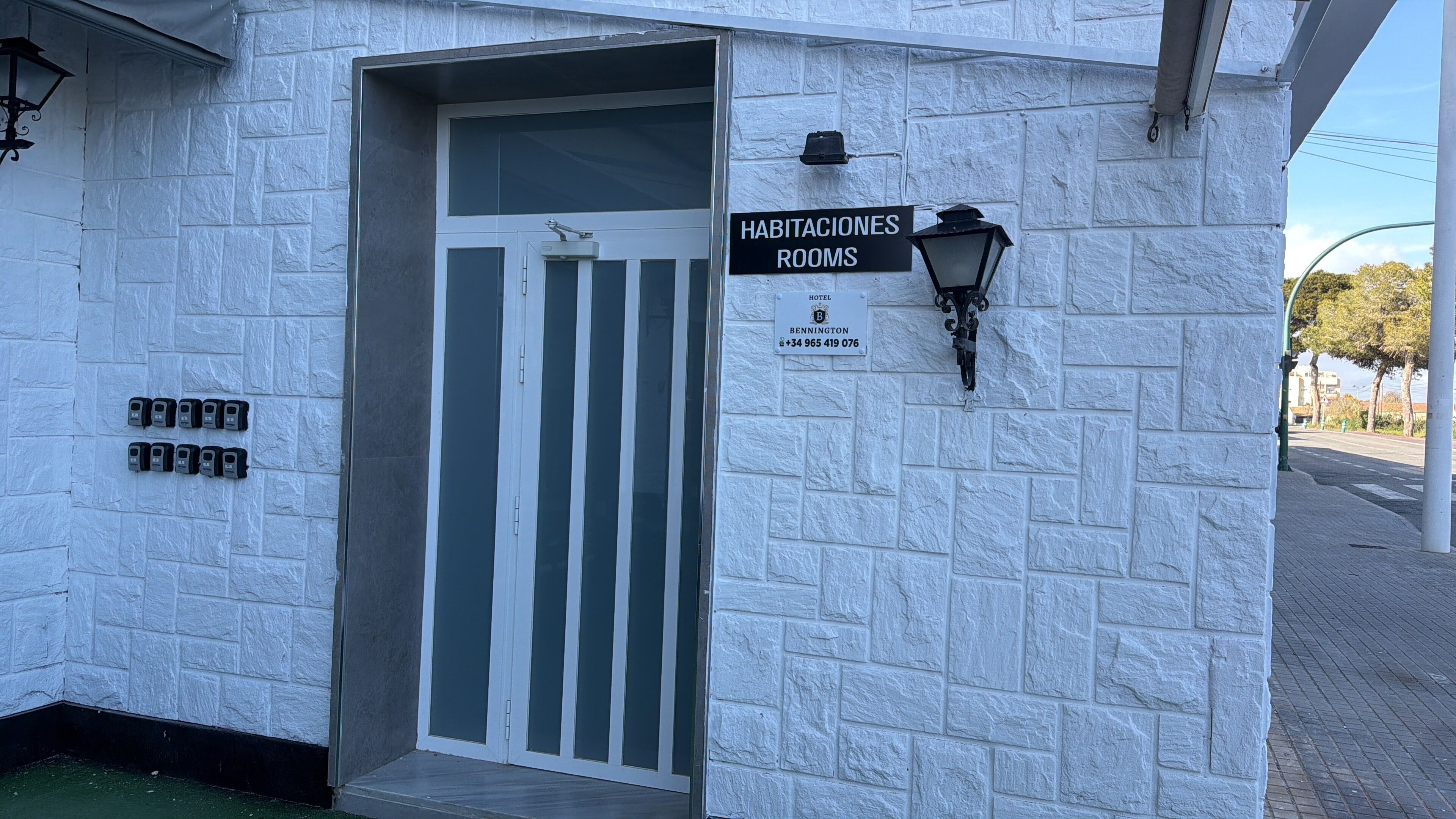 L’entrée d’un hôtel, avec une enseigne indiquant « HABITACIONES ROOMS » et un numéro de téléphone.