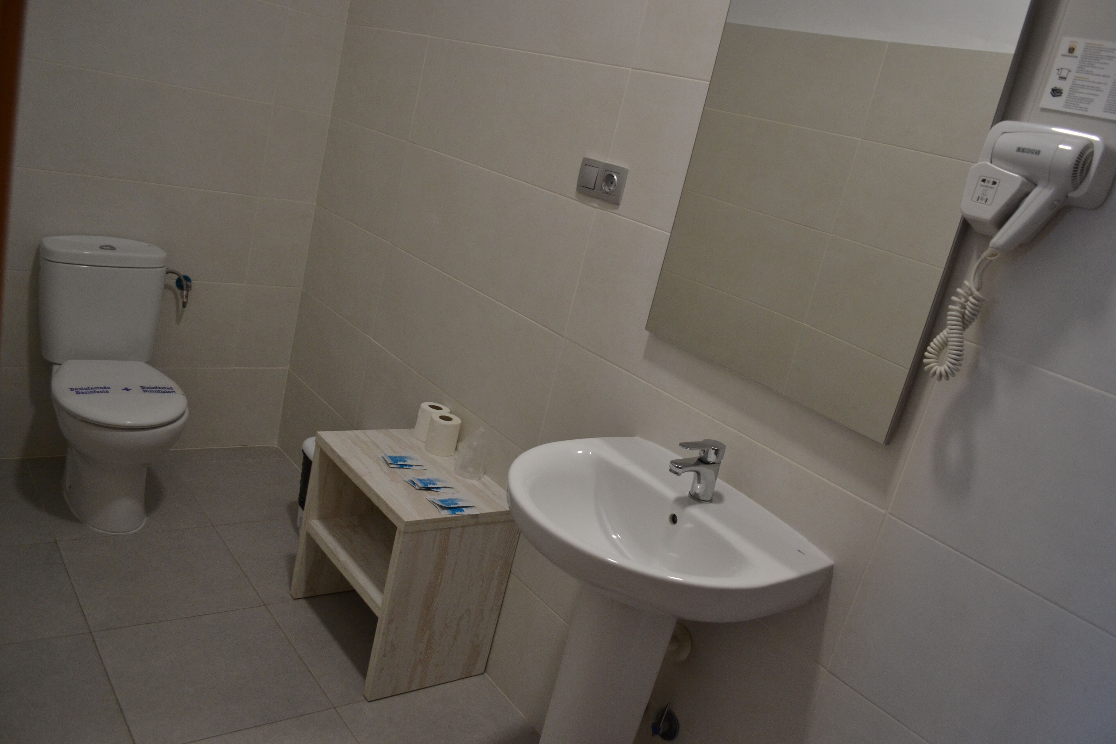 A bathroom with a toilet, a sink, and a hairdryer mounted on the wall.