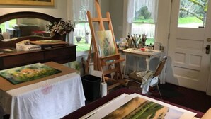 Un atelier d’art bien éclairé, avec un grand chevalet, un bureau rempli de matériel de peinture et un tableau en cours de réalisation.