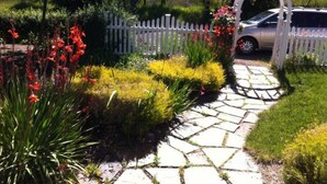 Un chemin de pierres menant à une porte blanche, entouré d’une végétation luxuriante et de plantes en fleurs.
