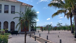 Un edificio con ventanas arqueadas y techo de tejas, rodeado de palmeras y un camino de grava.