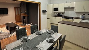 Una cocina moderna con armarios blancos, un comedor con mesa preparada para cuatro personas, y un horno empotrado.