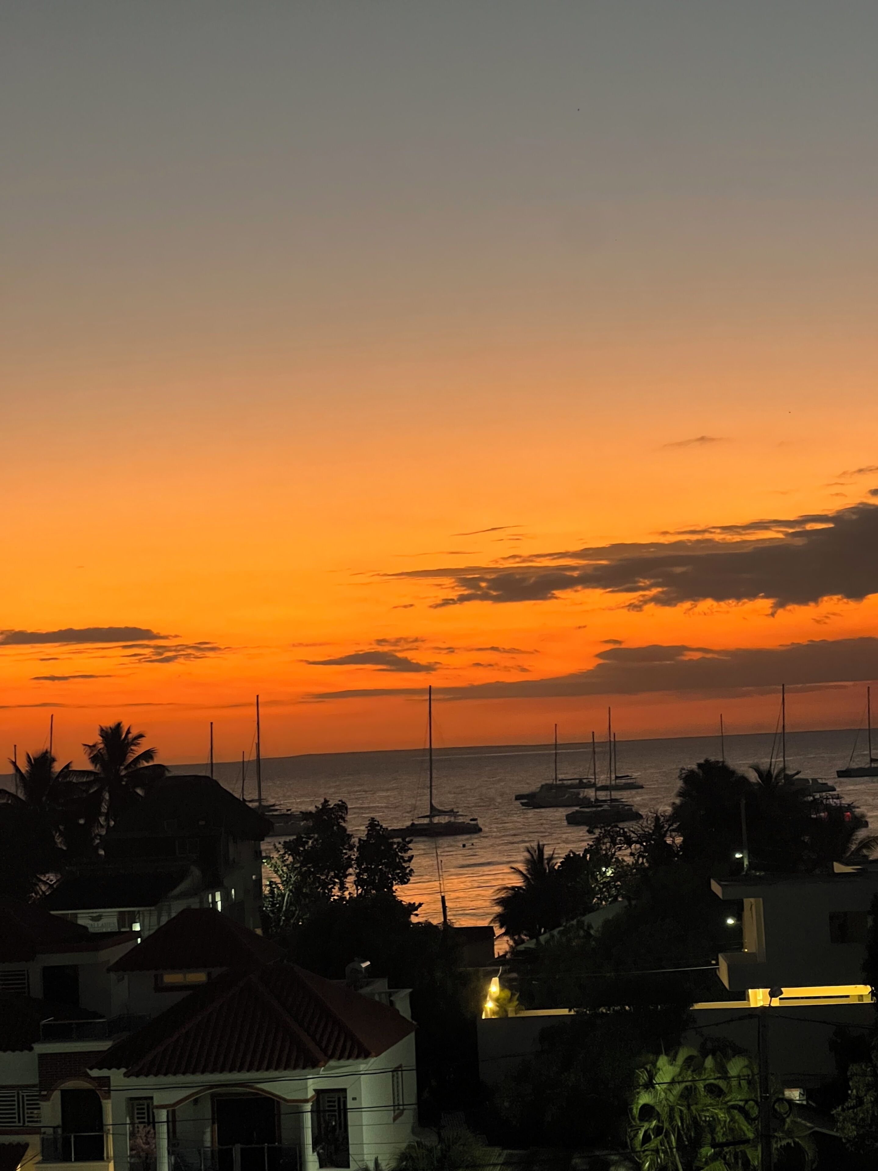 Atardecer costero con barcos y casas.
