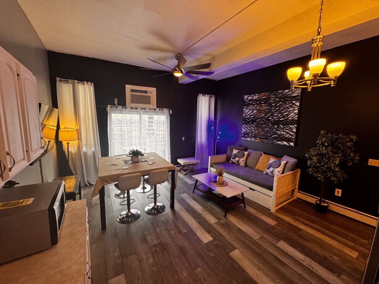A modern living room with a dining area, a ceiling fan, and a chandelier.