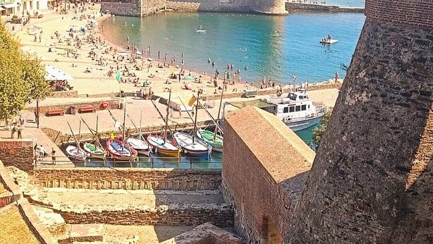 A coastal town with a historic fort, a sandy beach, and boats docked near the shore.