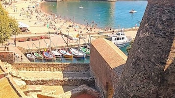 Un pueblo costero con un fuerte histórico, una playa de arena y barcos amarrados cerca de la orilla.