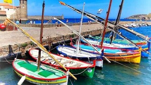 A harbor with several colorful boats docked, a stone building with a tower, and a clear blue sky.