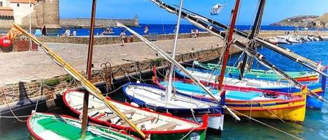 Un port où sont amarrés plusieurs bateaux aux couleurs vives, un bâtiment en pierre doté d’une tour et un ciel bleu clair.